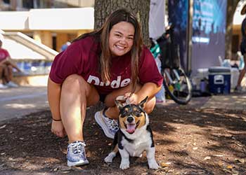 Texas A&M student in front a tree holding a small dog.