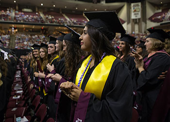 Texas A&M University student wearing graduation regalia sitting with other graduates at the graduation ceremony.