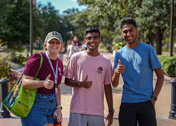 Three students at Texas A&M University standing together giving a thumbs up signal with their hands.