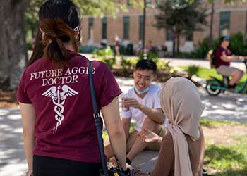 Texas A&M students talking outside. One student is wearing a shirt that displays Future Aggie Doctor.